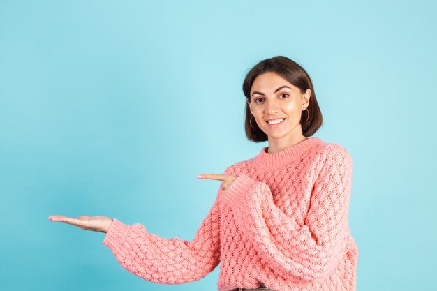 Jeune brune en pull rose isolé sur mur bleu