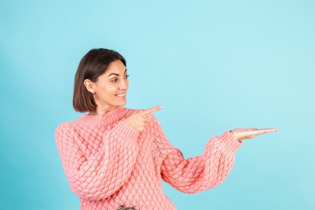 Jeune brune en pull rose isolé sur mur bleu