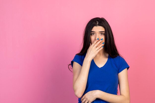 Jeune brune tenant sa main à sa bouche et regardant la caméra