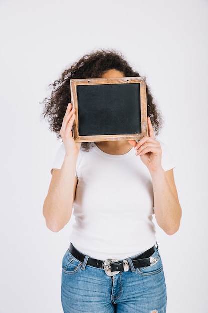 Photo gratuite jeune brunette se cachant le visage derrière le tableau noir