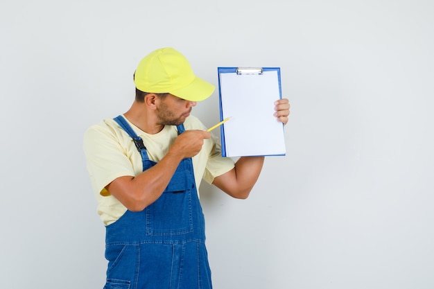 Jeune chargeur montrant quelque chose sur le presse-papiers en uniforme, vue de face.