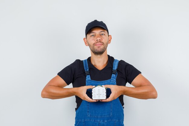 Jeune chargeur tenant le modèle de maison en uniforme, vue de face.