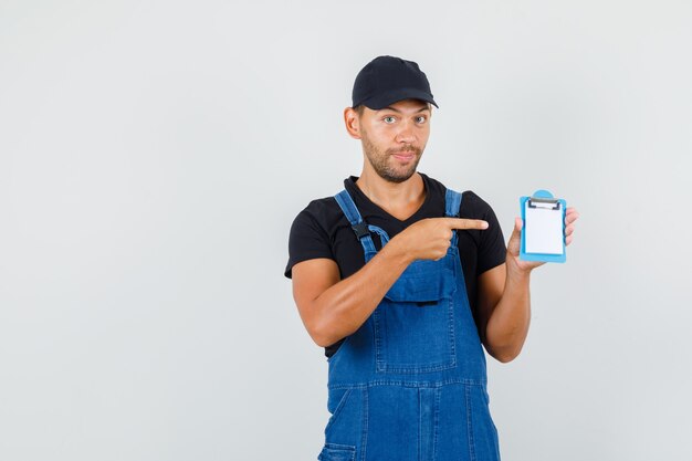 Jeune chargeur en uniforme pointant sur mini presse-papiers, vue de face.