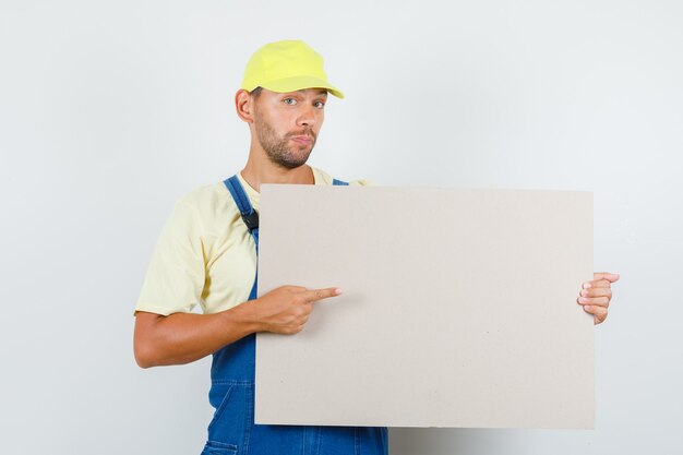 Jeune chargeur en uniforme pointant sur toile vierge, vue de face.