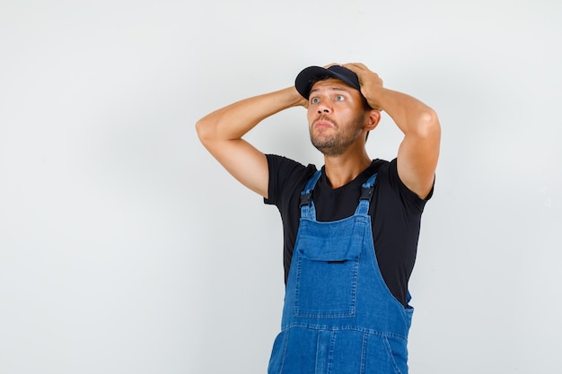 Photo gratuite jeune chargeur en uniforme regardant avec les mains sur la tête et à la confusion, vue de face.