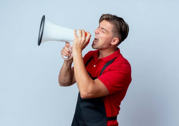 Jeune coiffeur homme blond ennuyé en uniforme crie dans haut-parleur isolé sur fond blanc avec copie espace