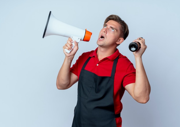 Jeune Coiffeur Homme Blond Ennuyé En Uniforme Détient Haut-parleur Et Vaporisateur à La Recherche D'isolement Sur L'espace Blanc Avec Copie Espace