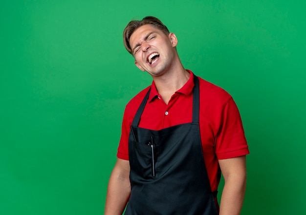 Jeune coiffeur homme blond ennuyé en uniforme isolé sur un espace vert avec copie espace