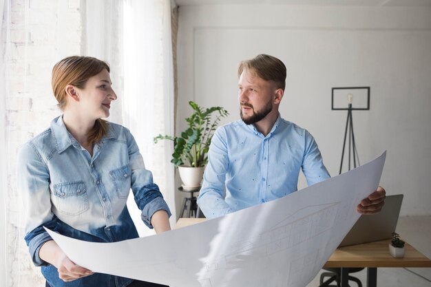 Jeune collègue masculin et féminin se regardant tout en maintenant le plan d&#39;action au bureau