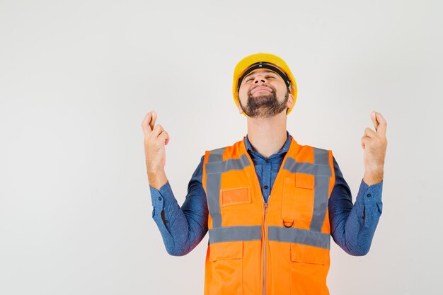 Jeune Constructeur Gardant Les Doigts Croisés En Chemise, Gilet, Casque Et à La Recherche De Calme. Vue De Face.