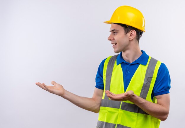 Jeune constructeur homme portant des uniformes de construction et un casque de sécurité sourit et demande