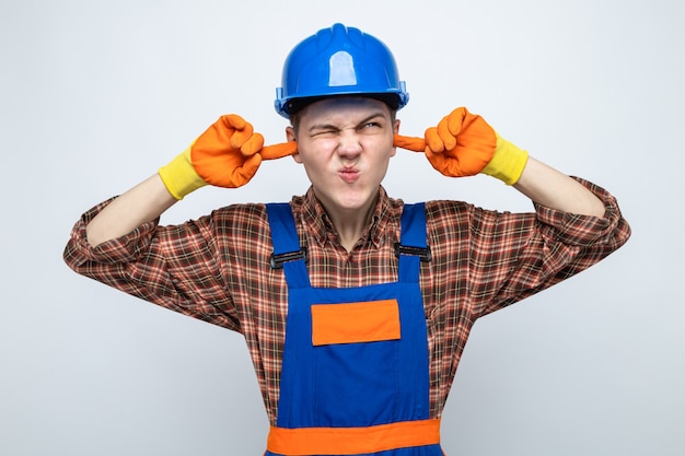 Photo gratuite jeune constructeur masculin en uniforme avec des gants isolé sur mur blanc