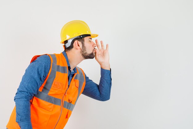 Jeune constructeur montrant un geste délicieux en chemise, gilet, casque et à la recherche de plaisir. .