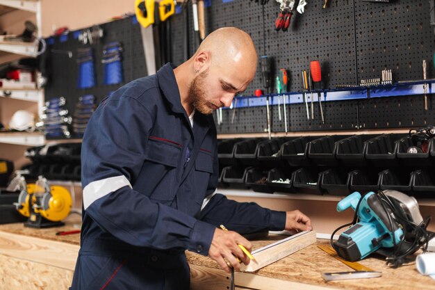 Jeune contremaître en vêtements de travail à l'aide d'une règle avec une variété d'outils sur fond d'atelier