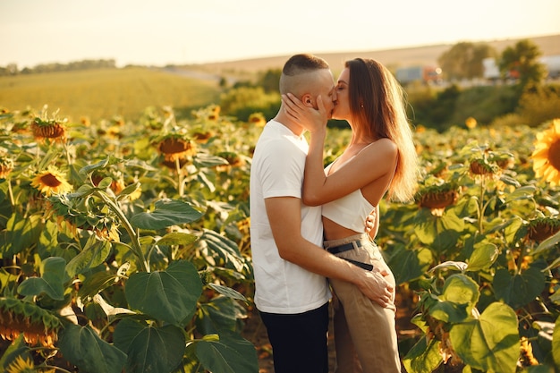 Jeune couple aimant s'embrasse dans un champ de tournesol. Portrait de couple posant en été dans le champ.