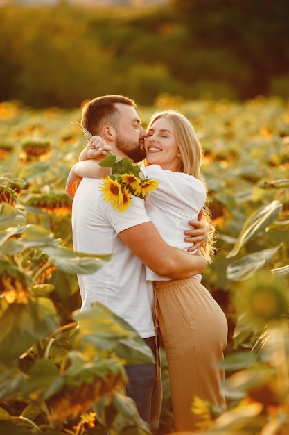 Jeune couple aimant s'embrasse dans un champ de tournesol. Portrait de couple posant en été dans le champ.