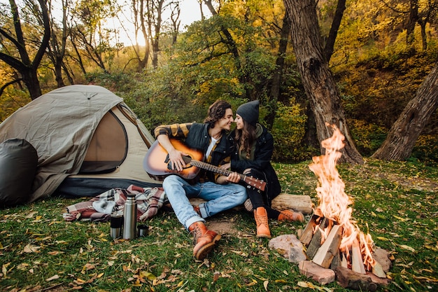 Photo gratuite jeune couple aimant de touristes se détendre près du feu dans la nature