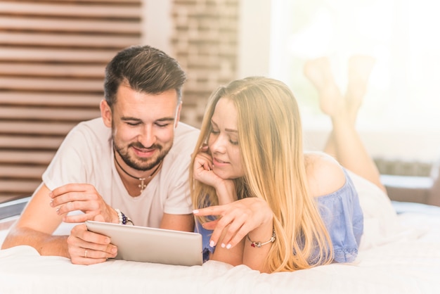 Jeune couple allongé sur un lit douillet en regardant tablette numérique