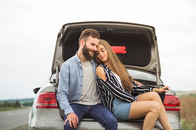 Jeune couple d&#39;amoureux assis dans le coffre de la voiture