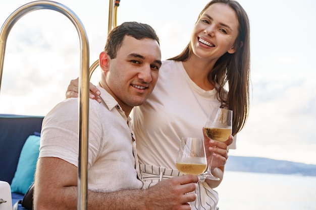 Jeune couple d'amoureux assis sur le pont du yacht et buvant du vin