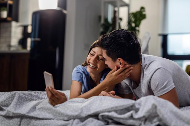 Jeune couple d'amoureux s'amusant tout en prenant un selfie avec un téléphone intelligent dans la chambre