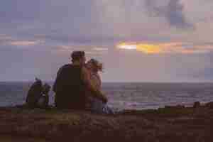 Photo gratuite un jeune couple amoureux en voyage est assis au bord d'une falaise et regarde le coucher du soleil.