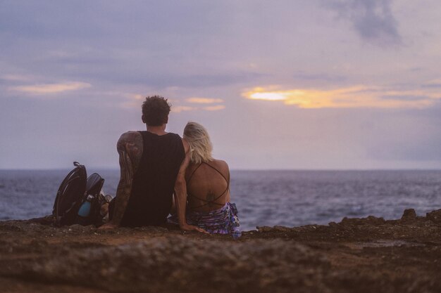 Un jeune couple amoureux en voyage est assis au bord d'une falaise et regarde le coucher du soleil.