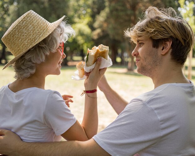 Jeune couple appréciant des hamburgers dans le parc ensemble