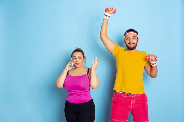 Jeune couple assez caucasien dans des vêtements lumineux formation sur l'espace bleu Concept de sport, émotions humaines, expression, mode de vie sain, relation, famille