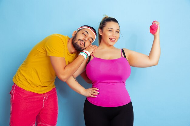 Jeune couple assez caucasien dans des vêtements lumineux formation sur l'espace bleu Concept de sport, émotions humaines, expression, mode de vie sain, relation, famille