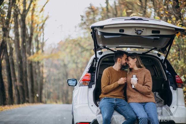 Jeune couple assis à l'arrière d'une voiture, buvant du thé en forêt