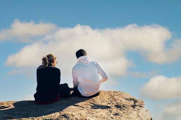Jeune couple assis au sommet d'une falaise sous un ciel nuageux