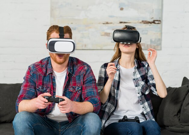 Jeune couple assis sur le canapé pendant l&#39;expérience vr jouant le joystick