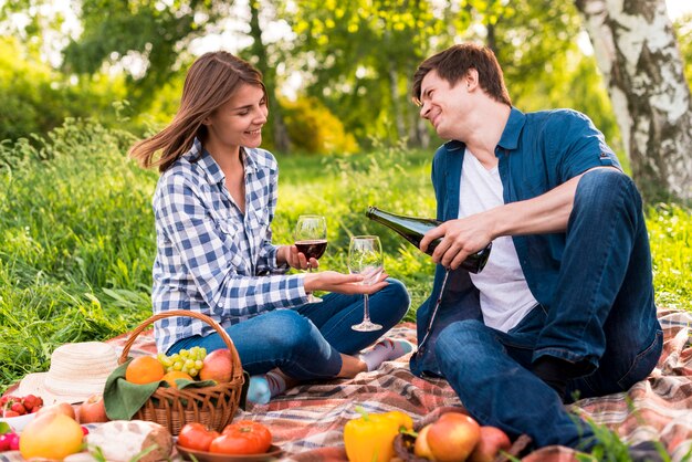 Jeune couple assis sur une couverture et verser du vin