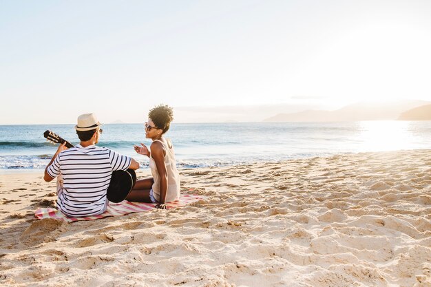 Jeune couple assis à la plage et jouant de la guitare