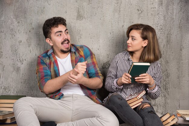 jeune couple assis et prenant un livre l'un de l'autre