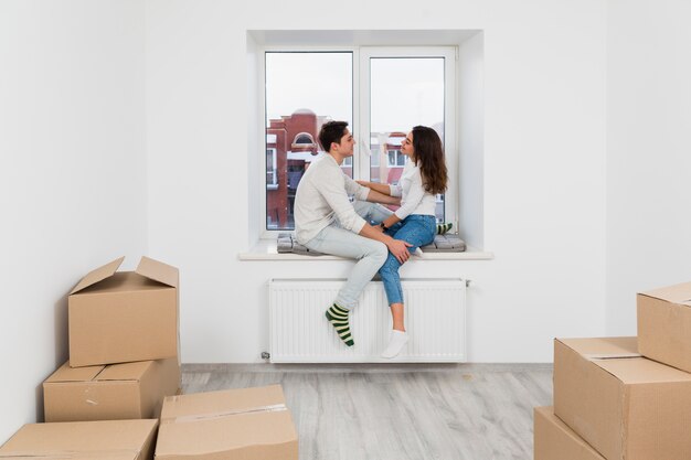 Jeune couple assis sur le rebord de la fenêtre profitant d&#39;un nouvel appartement