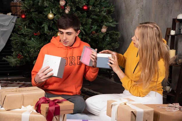 Jeune couple assis sur le sol et considérant des cadeaux à l'intérieur de Noël