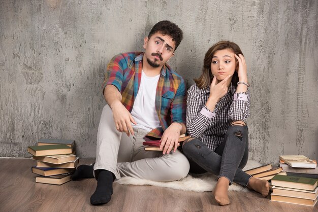 Jeune couple assis sur le sol avec des livres et de la pensée