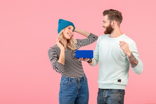 Jeune couple attrayant écoutant de la musique sur un haut-parleur sans fil portant une tenue élégante cool souriant heureux humeur positive posant sur fond rose isolé dansant s'amusant