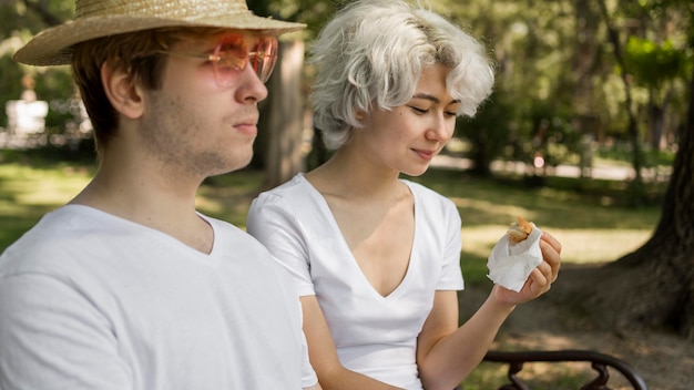 Jeune couple au parc de manger des hamburgers ensemble