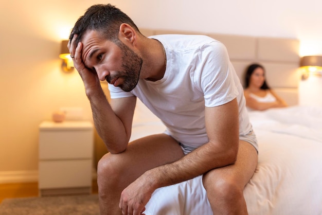 Jeune couple ayant un problème Guy est assis sur le lit et regarde tristement sa petite amie en arrière-plan Bouleversé jeune couple ayant des problèmes avec le sexe
