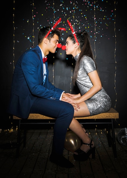 Jeune couple avec bandeaux en bois de cerf et nez rigolo entre des confettis
