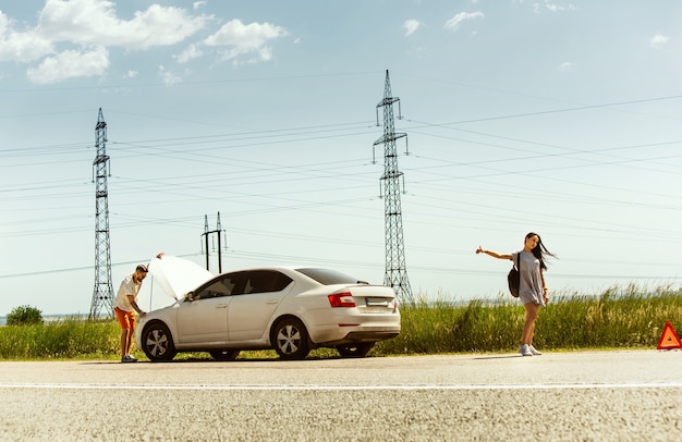 Photo gratuite le jeune couple a cassé la voiture alors qu'il se rendait au repos. ils essaient d'arrêter les autres conducteurs et demandent de l'aide ou font de l'auto-stop