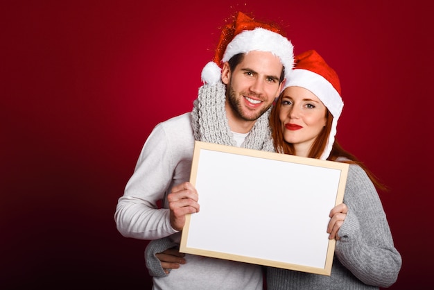 Jeune couple avec un chapeau de Santa tenant un tableau blanc