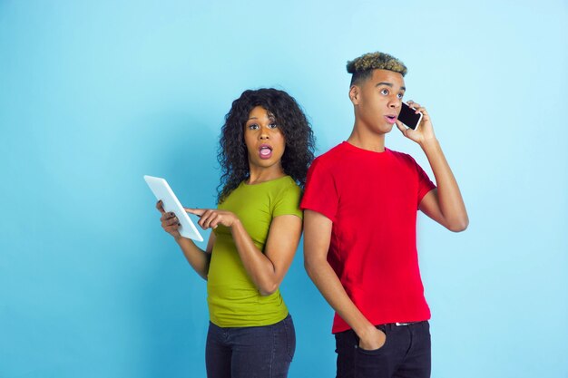 Jeune couple choqué dans des vêtements décontractés posant sur le mur bleu