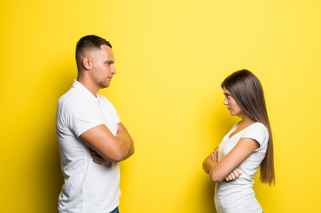 Jeune couple en colère vêtu de t-shirts blancs à la recherche l'un de l'autre sur fond jaune