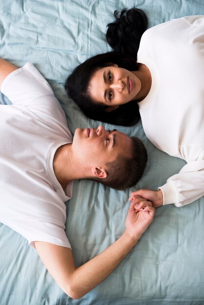 Jeune couple, dans, blanc, vêtements, coucher lit tête tête tête, et, tenant mains