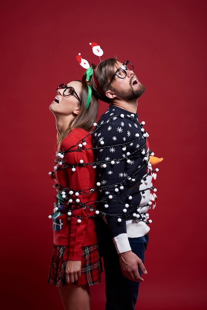 Jeune couple dans des vêtements de Noël étranges attachés avec des lumières de Noël