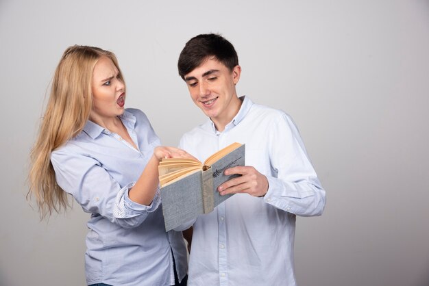 Jeune couple debout et lisant un livre sur fond gris